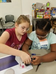 Two young girls working together to try apart a toy.