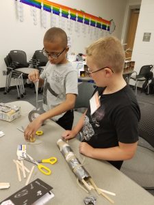 Two boys working together with tape, scissors and other materials. 